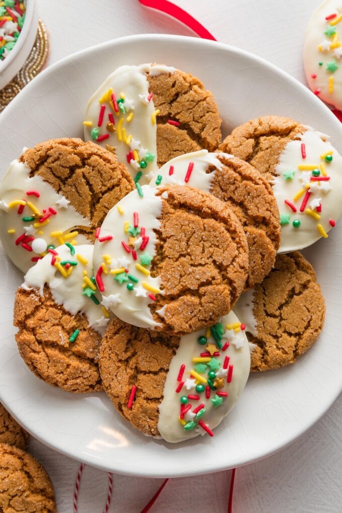 Plate of white chocolate dipped ginger cookies with Christmas-themed sprinkles.