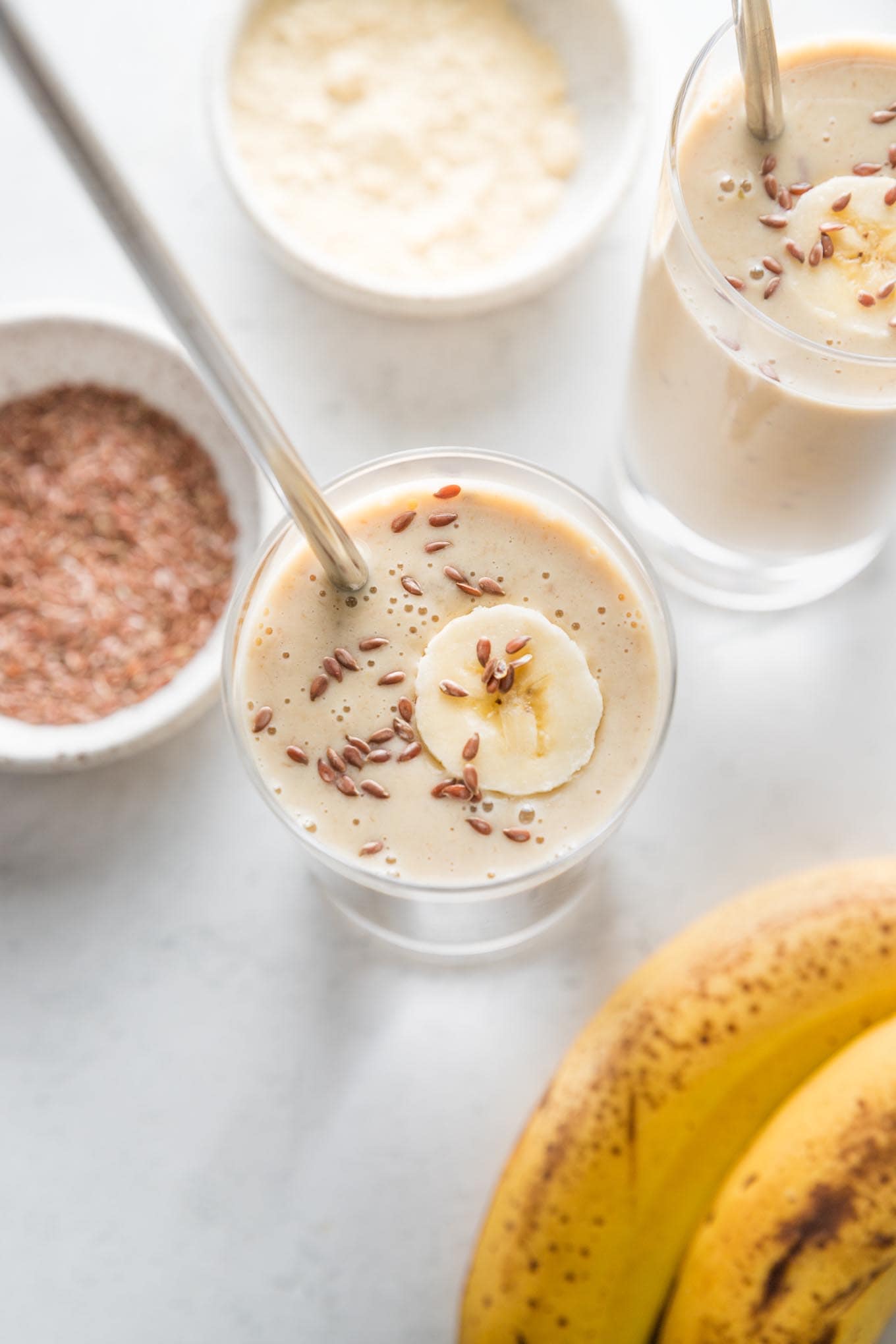 Overhead view of two simple banana protein shakes with almond milk and flaxseeds, in glasses and ready to be enjoyed.