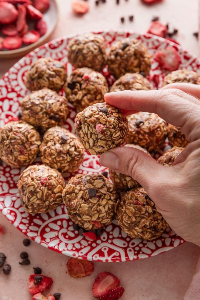 Close up of a woman's hand picking up a small chocolate strawberry-flavored protein bite snack.