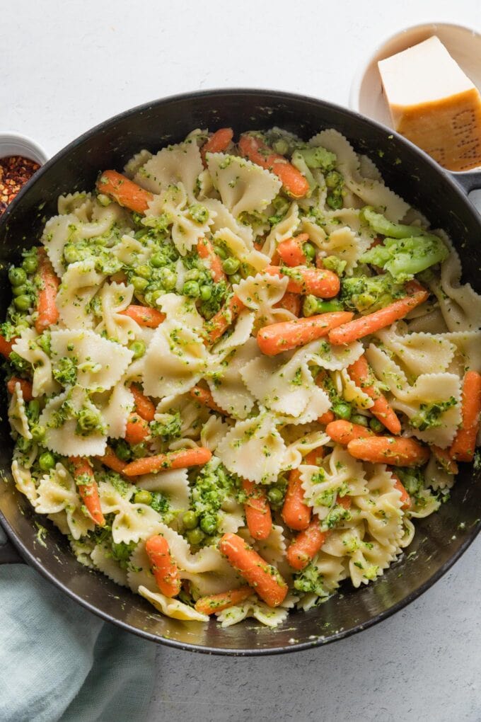Large pan full of pasta with broccoli, baby carrots, and peas.