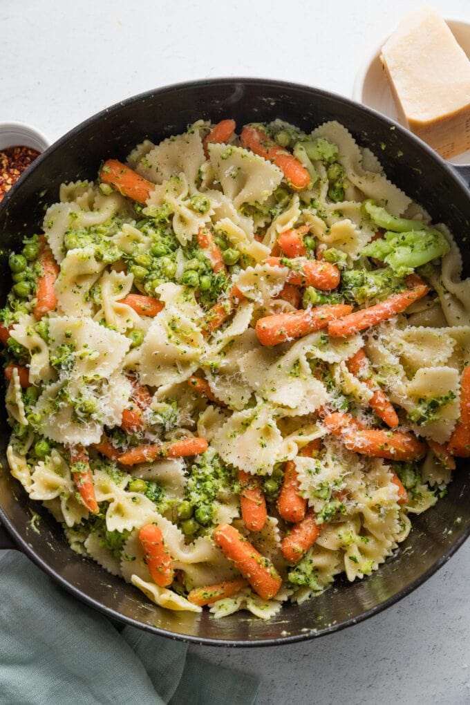 A generous amount of grated Parmesan and black pepper sprinkled on top of a pan of broccoli carrot pasta with lemon garlic sauce.