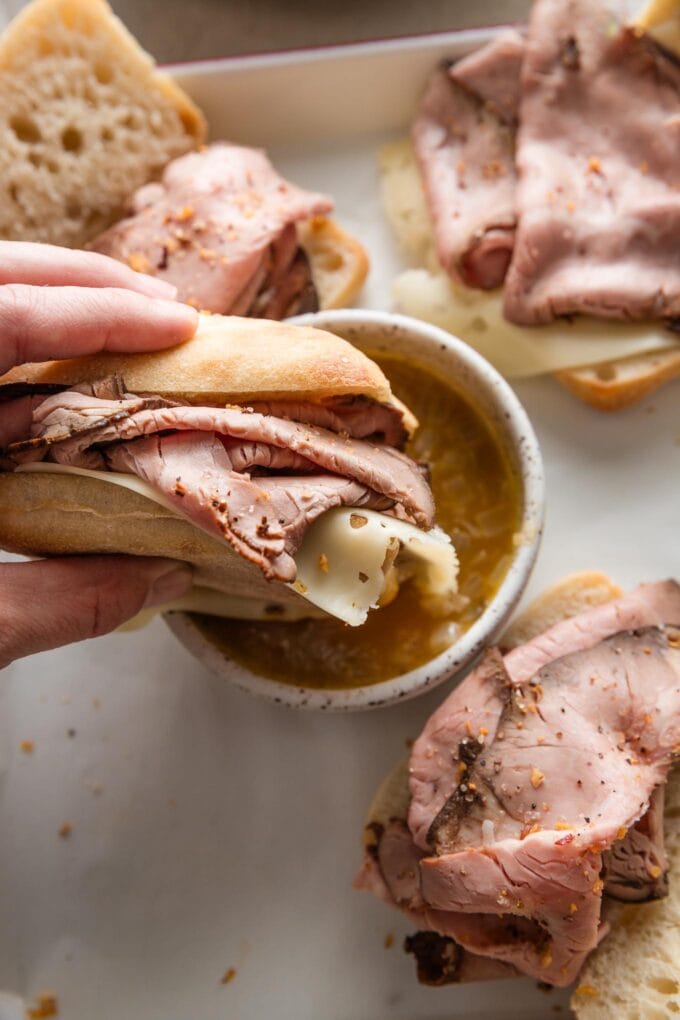 Hand dipping a small French dip sandwich into a quick homemade au jus.