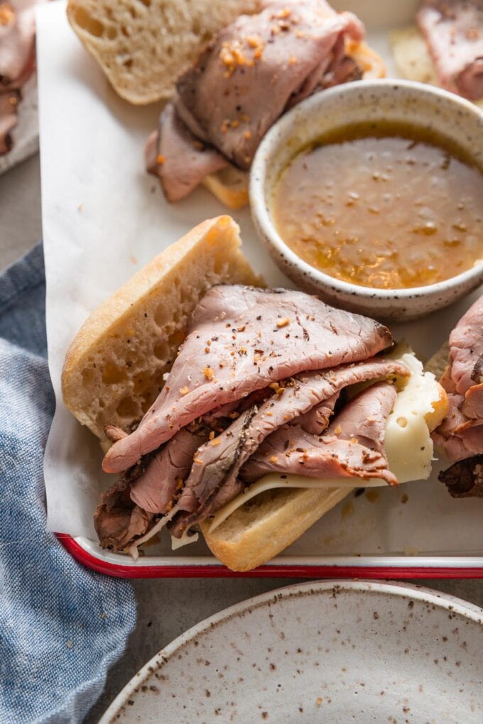 Close up angled view of a small French dip sandwich with au jus for dipping in the background.