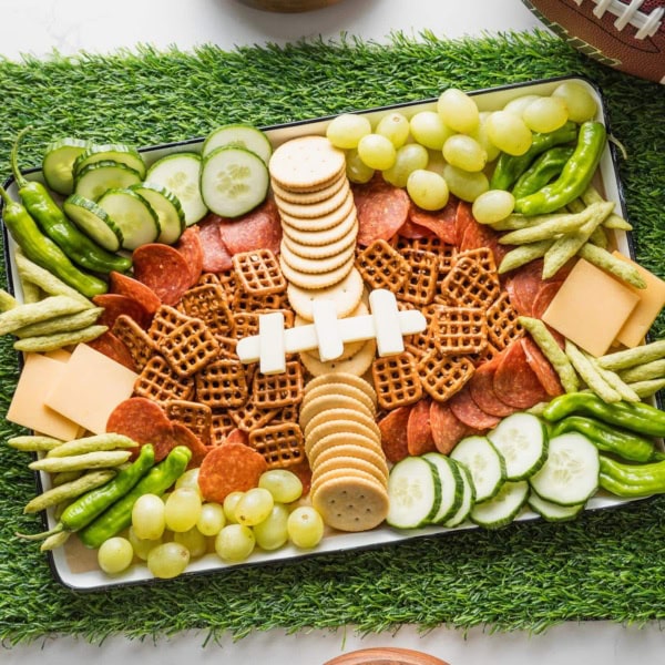 Overhead view of a snack tray with brown, green, and white snacks shaped a bit like a football, set on a table runner made of artificial green turf.