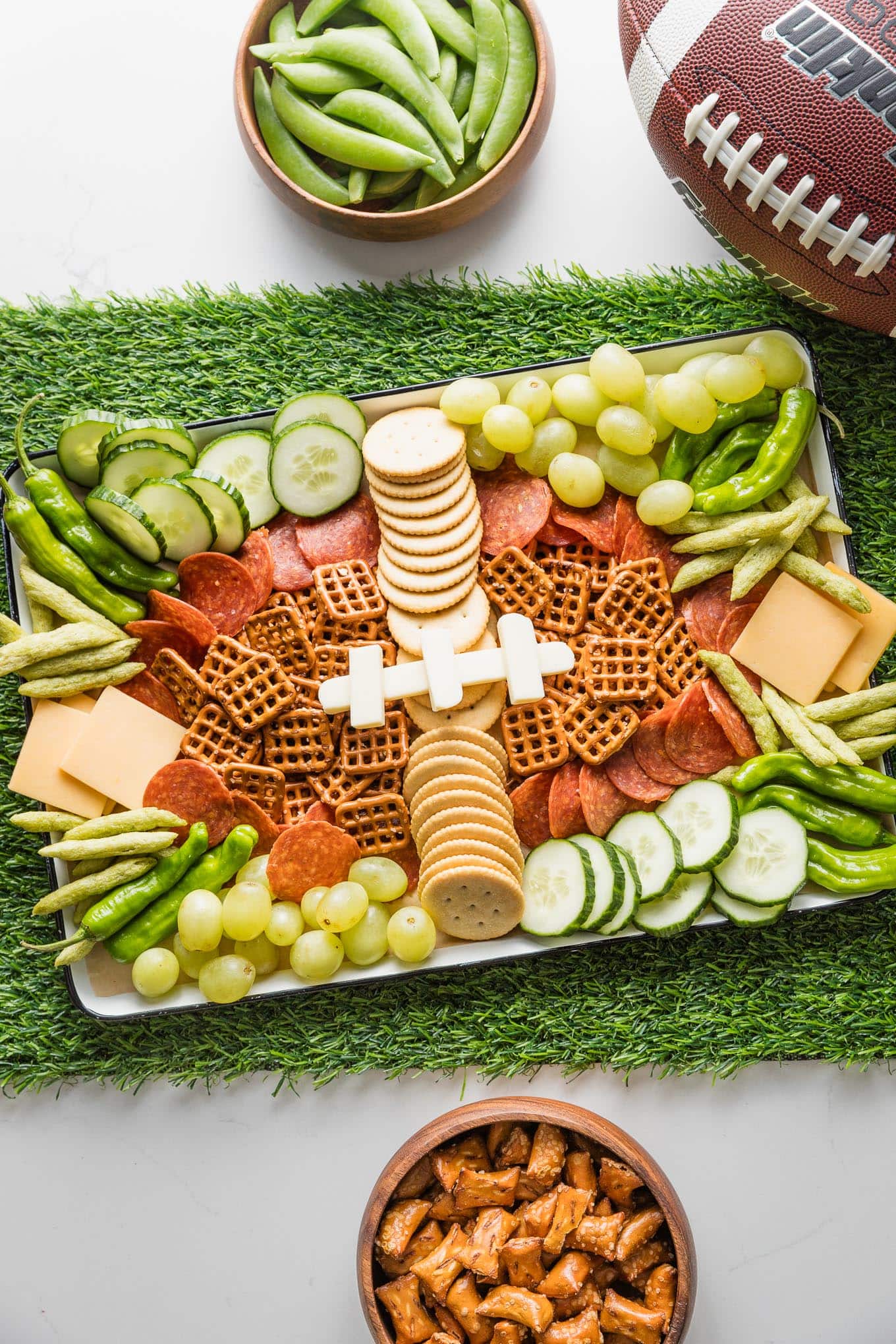 Overhead view of a snack tray with brown, green, and white snacks shaped a bit like a football, set on a table runner made of artificial green turf.