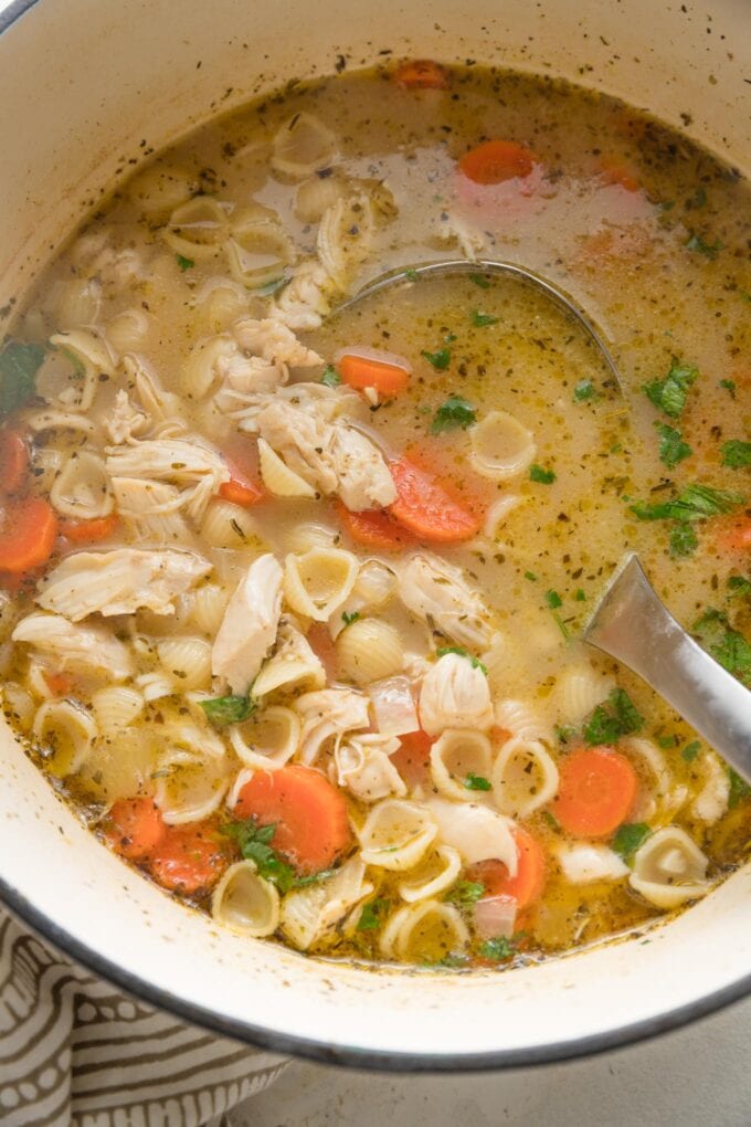 Large pot of lemon chicken soup with a ladle stirring a large spoonful.