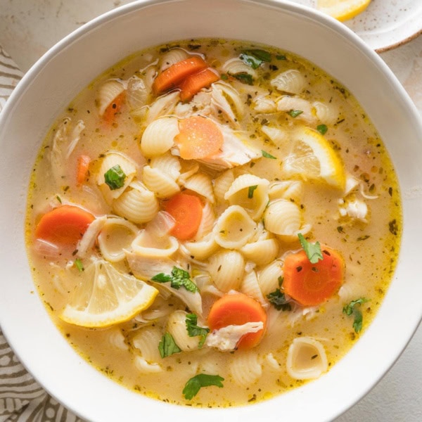 Close up bowl full of lemon chicken soup with pasta, carrots, parsley, and a rich broth.