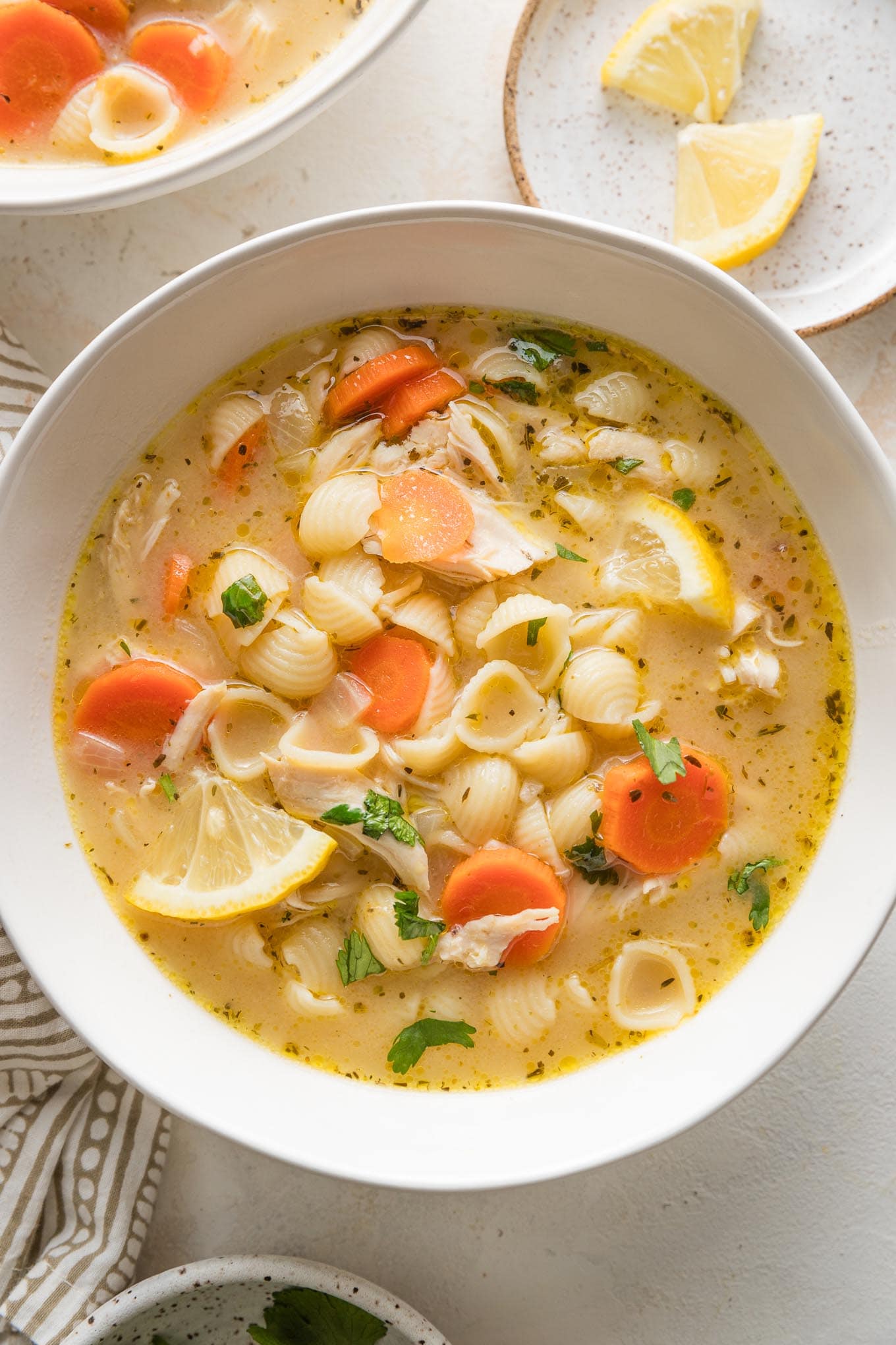 Close up bowl full of lemon chicken soup with pasta, carrots, parsley, and a rich broth.