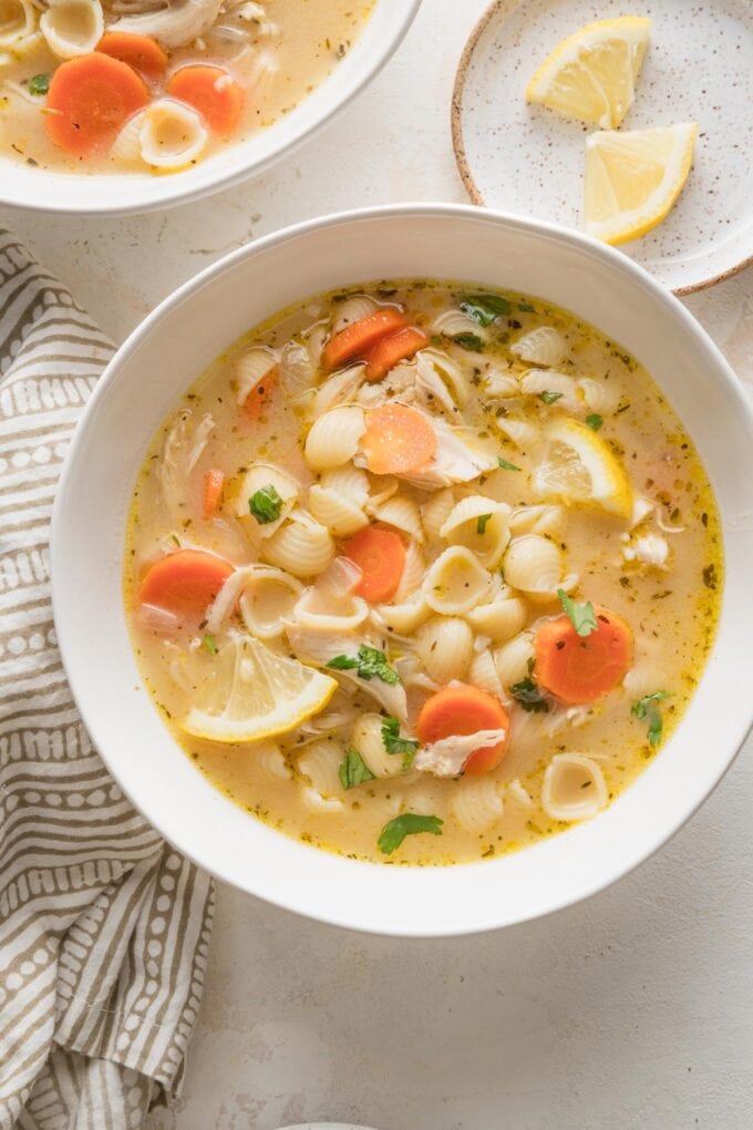 Countertop set with two bowls of lemon chicken soup, with extra lemon wedges nearby for extra citrus flavor.