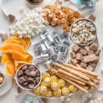 Large white platter filled with candy, dried fruit, and Pirouette cookies in silver, gold, and white tones, for celebrating New Year's Eve.