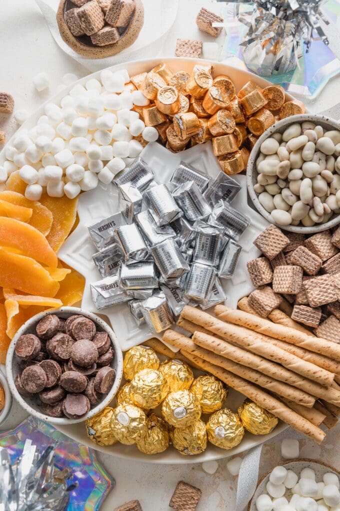 Close up of a New Year's-themed candy board with gold, silver, white, and chocolate candies.