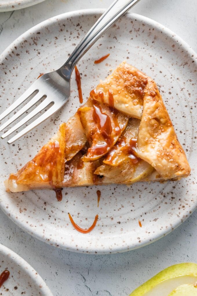 Close up of a slice of pear caramel galette with extra caramel sauce, served on a small ceramic plate.