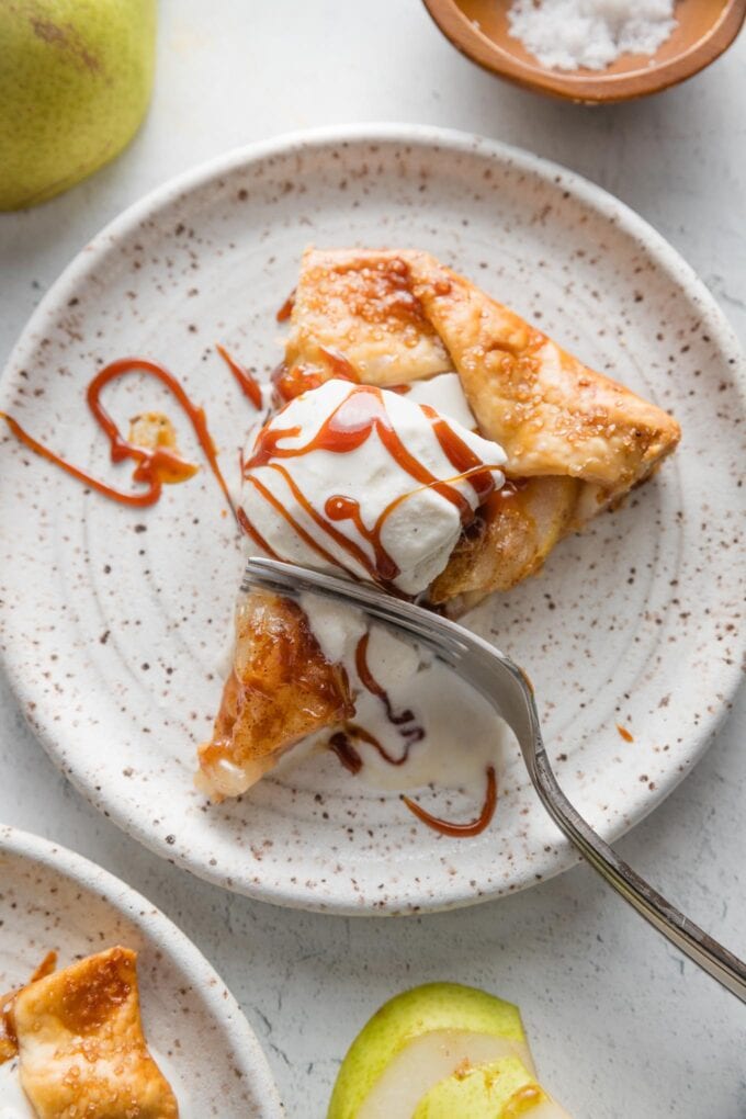Slice of pear caramel galette served with a scoop of vanilla ice cream and an extra drizzle of salted caramel sauce.