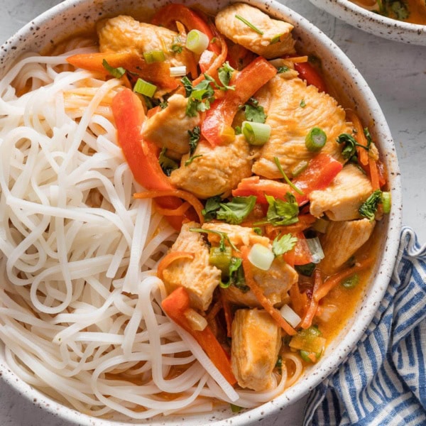 Small ceramic bowl full of a homemade Thai-inspired red chicken curry with rice noodles.