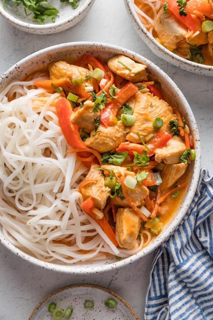Small ceramic bowl full of a homemade Thai-inspired red chicken curry with rice noodles.