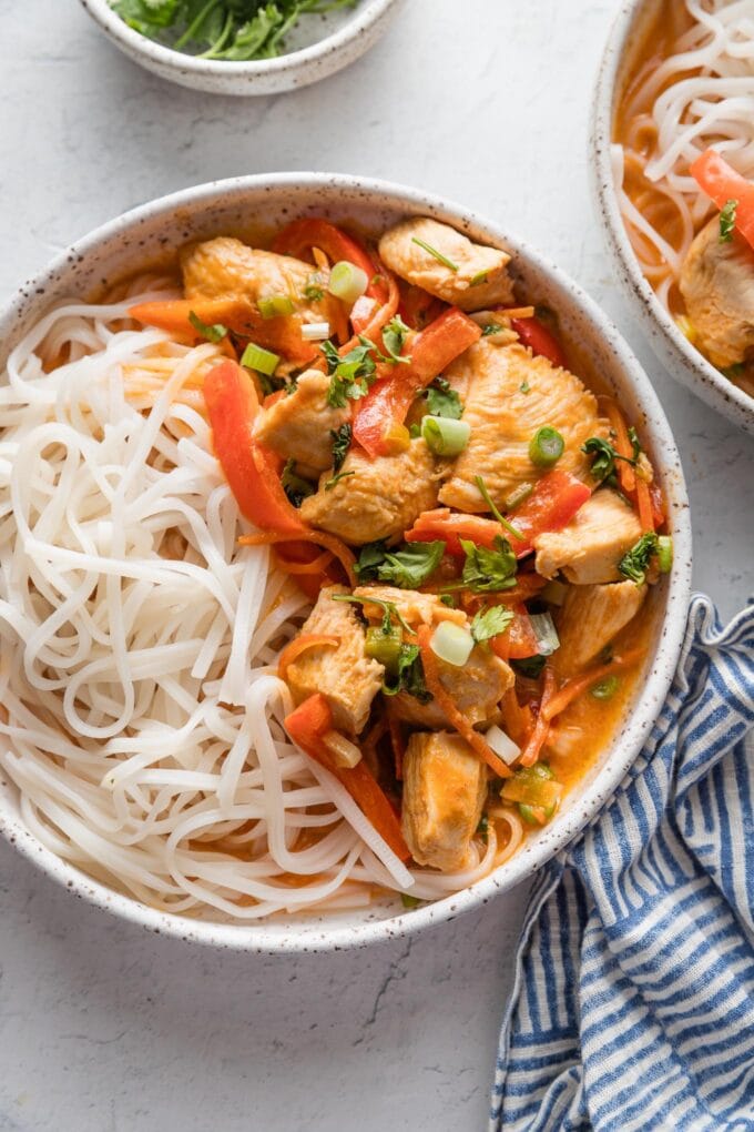 Countertop set with bowls of Thai inspired red chicken curry served with rice noodles.