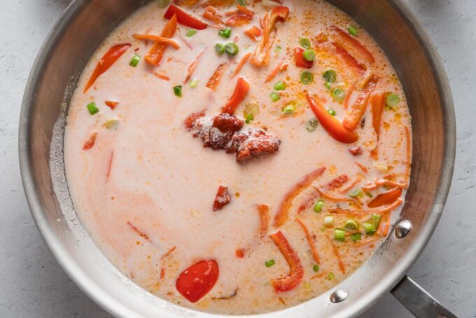 Red curry sauce being simmered in a skillet with veggies.