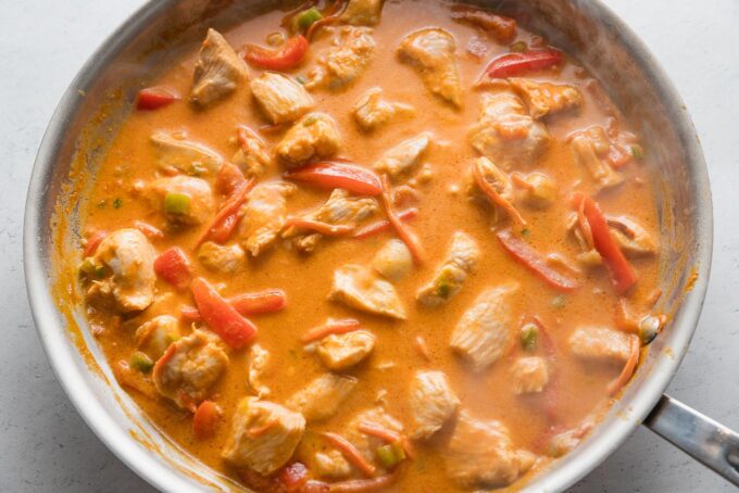 Thai red chicken curry just cooked in a skillet with red bell pepper and carrots.