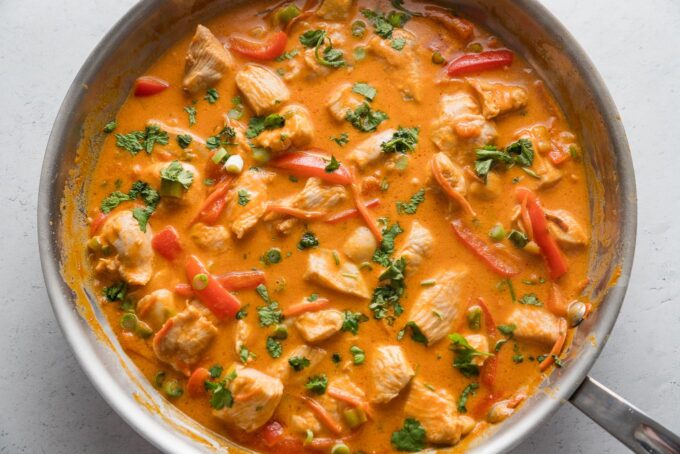Thai red curry chicken in a skillet topped with fresh cilantro and fresh chopped green onions.