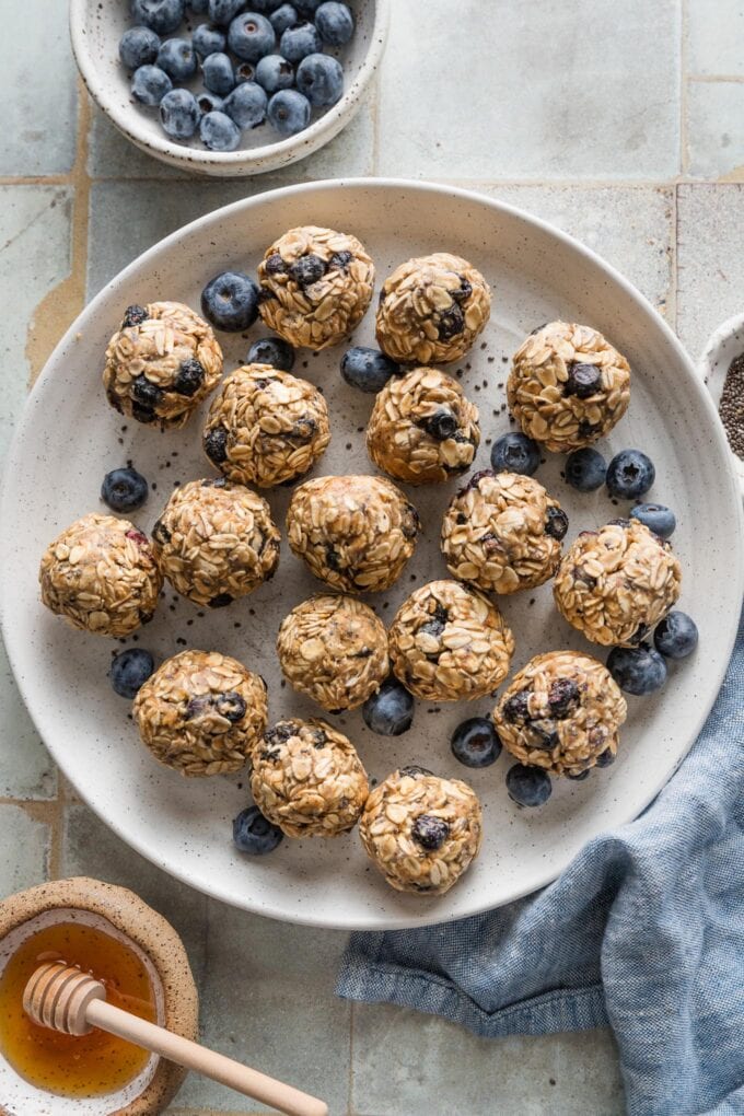White salad plate filled with rolled protein bites made of oats, freeze-dried blueberries, honey, nut butter, and chia seeds.