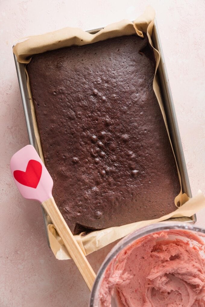 Chocolate sheet cake just removed from the oven, with a bowl of strawberry frosting ready nearby.