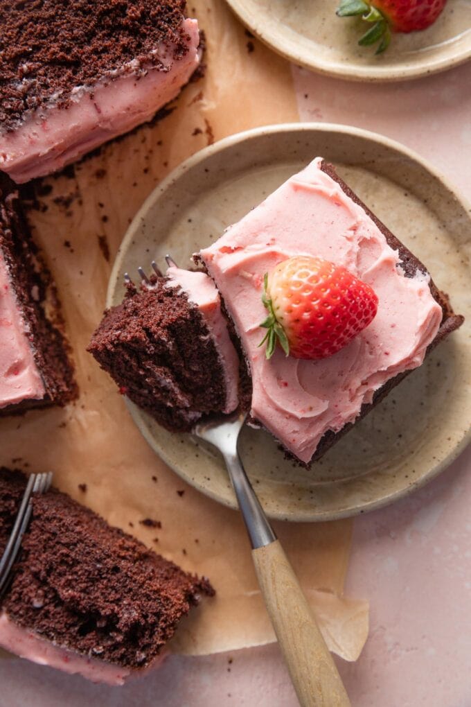 Small square of chocolate cake with strawberry frosting, with one forkful removed to take a bite.