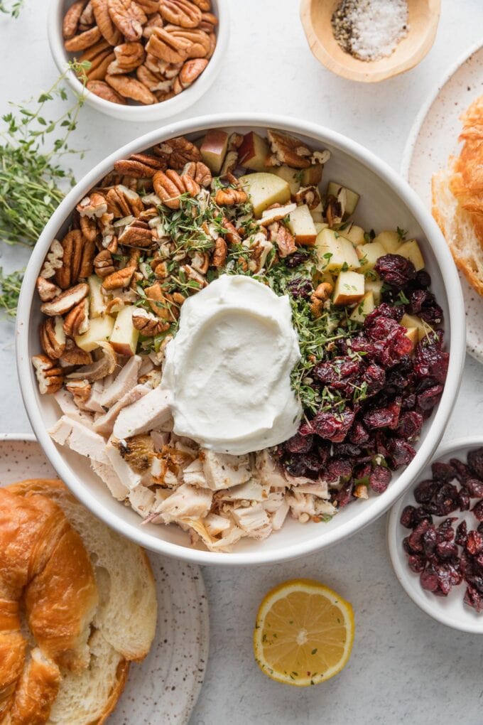 Bowl filled with the ingredients for a cranberry pecan chicken salad with Greek yogurt, added in quadrants but not yet mixed together.