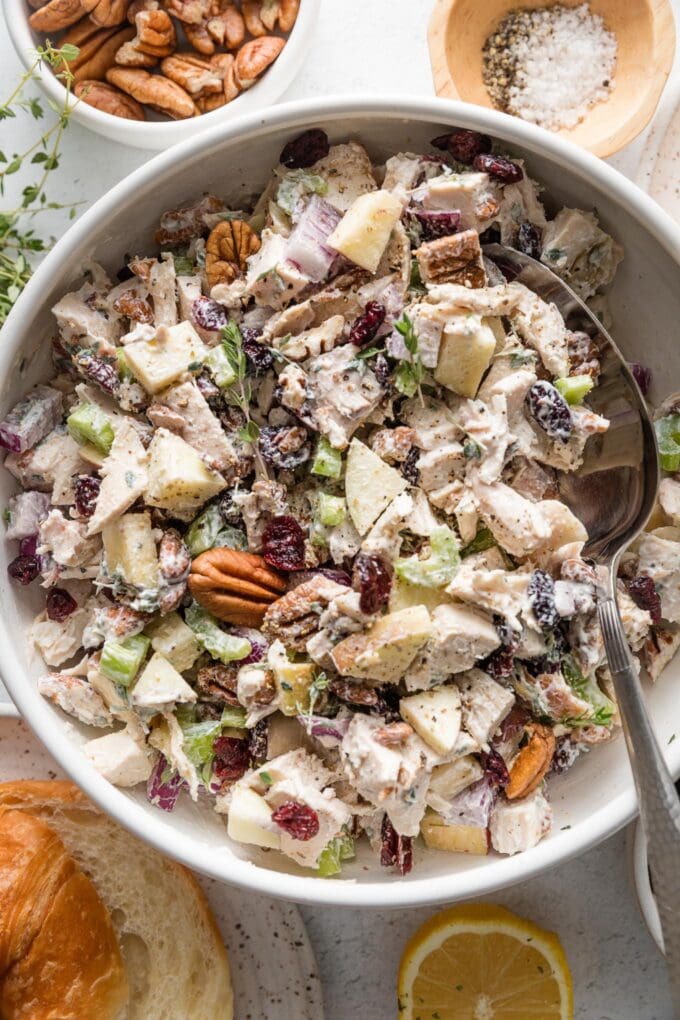 Close up view of a large serving spoon scooping out a portion of chicken salad made with Greek yogurt, dried cranberries, and toasted pecans.