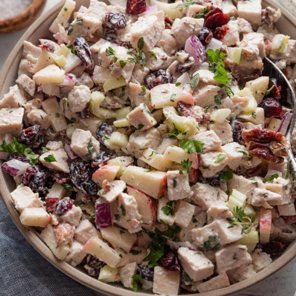 Bowl of cranberry pecan chicken salad with apples, celery, and fresh thyme.