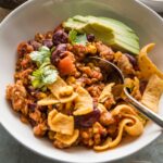 Close up of a spoonful of red chicken chili made with ground chicken and a homemade spice blend, topped with corn chips and sliced avocado.
