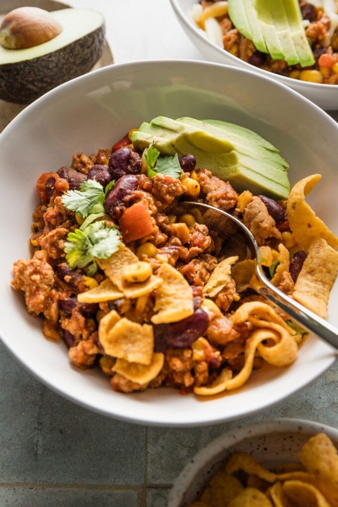 Close up of a spoonful of red chicken chili made with ground chicken and a homemade spice blend, topped with corn chips and sliced avocado.