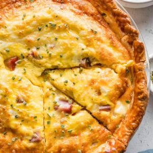 Close up of a ham and Swiss quiche with one slice cut out.