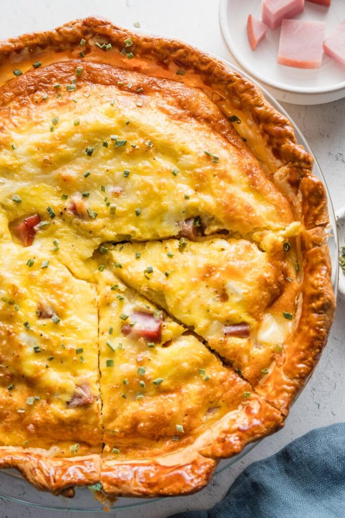 Close up of a ham and Swiss quiche with one slice cut out.