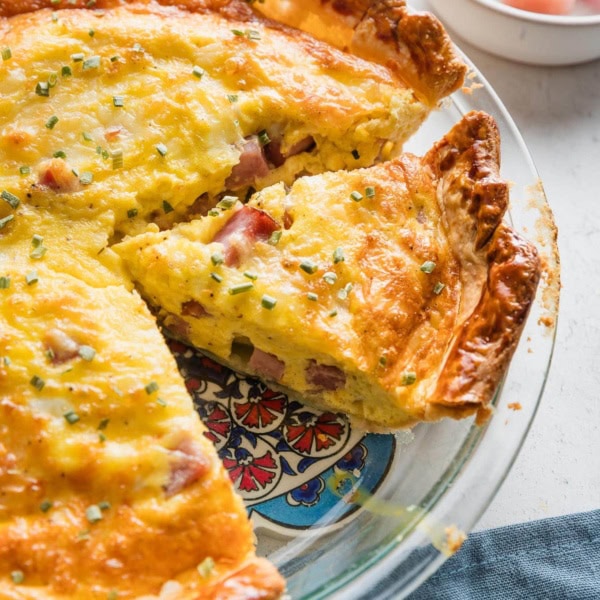 Pie plate with an easy ham and Swiss quiche, partially sliced to serve.