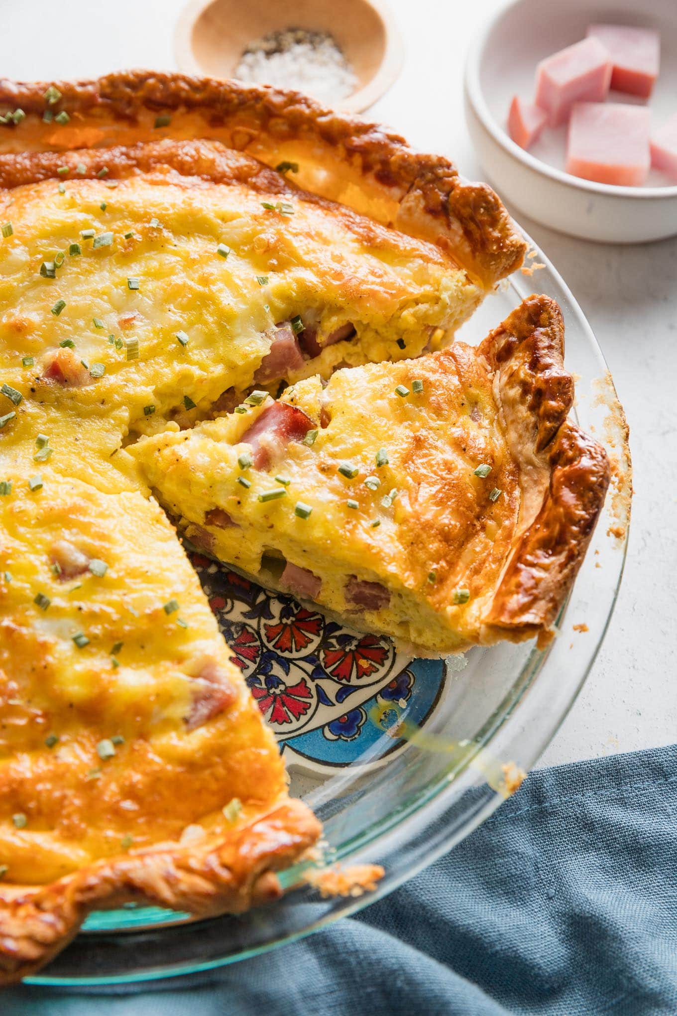 Pie plate with an easy ham and Swiss quiche, partially sliced to serve.
