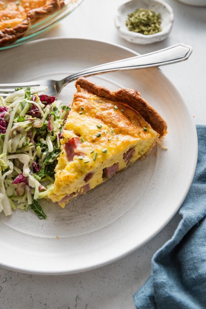 Small plate with a slice of ham and Swiss quiche served with a small salad.