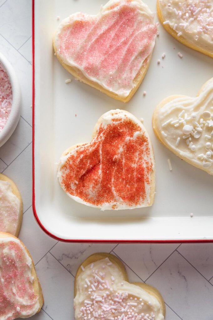 Red sprinkled, frosted heart shaped cut out sugar cookie on a tray, ready to eat.