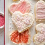 Close up of heart shaped cut out sugar cookies with spreadable frosting and a mix of pink, white, and red sprinkles.