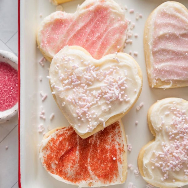 Close up of heart shaped cut out sugar cookies with spreadable frosting and a mix of pink, white, and red sprinkles.