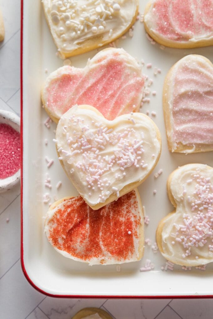 Close up of heart shaped cut out sugar cookies with spreadable frosting and a mix of pink, white, and red sprinkles.