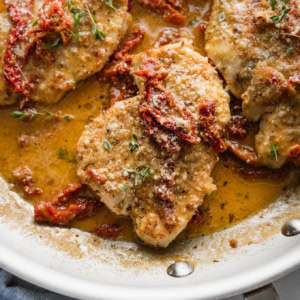 Close up of creamy sun dried tomato chicken breasts in a skillet with Parmesan and fresh herbs.