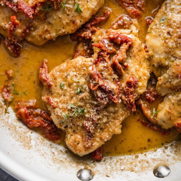 Close up of a chicken breast in creamy sun dried tomato sauce with Parmesan and fresh thyme.