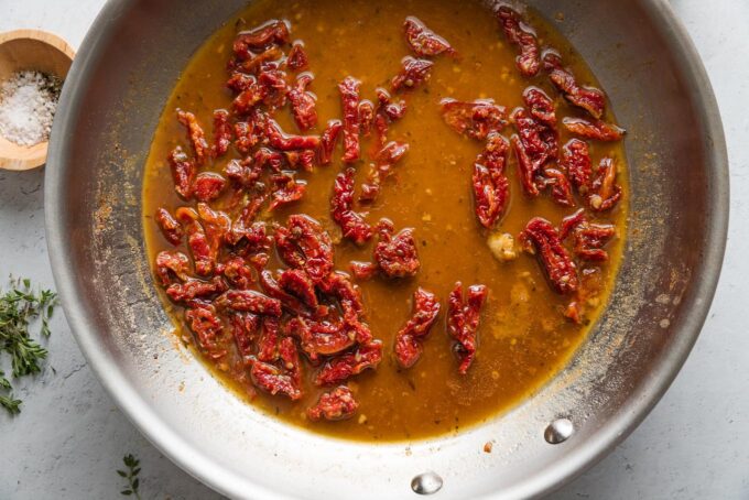 Julienned sun-dried tomatoes simmering in broth with garlic.