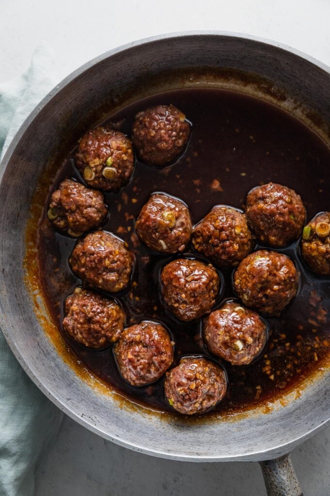 Deep cast iron skillet filled with Asian-inspired ground beef meatballs in a sweet and sticky homemade pan sauce.