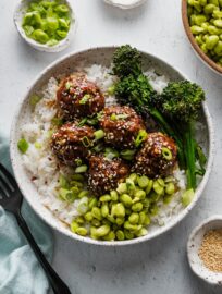 Rice bowl with sweet and sticky Asian meatballs, edamame, roasted broccolini, green onions, and toasted sesame seeds.
