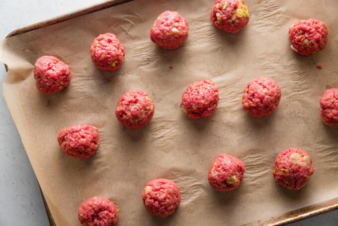 Meatball mixture portioned and rolled into balls and arranged on a parchment lined sheet pan.