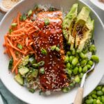 Close up overhead view of a teriyaki salmon bowl with carrot, cucumber, edamame, and rice.