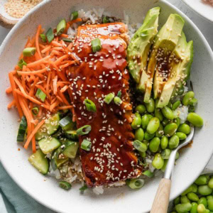 Close up overhead view of a teriyaki salmon bowl with carrot, cucumber, edamame, and rice.