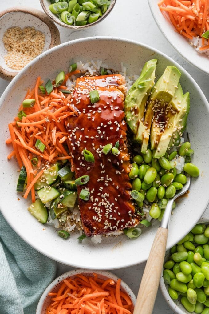 Close up overhead view of a teriyaki salmon bowl with carrot, cucumber, edamame, and rice.
