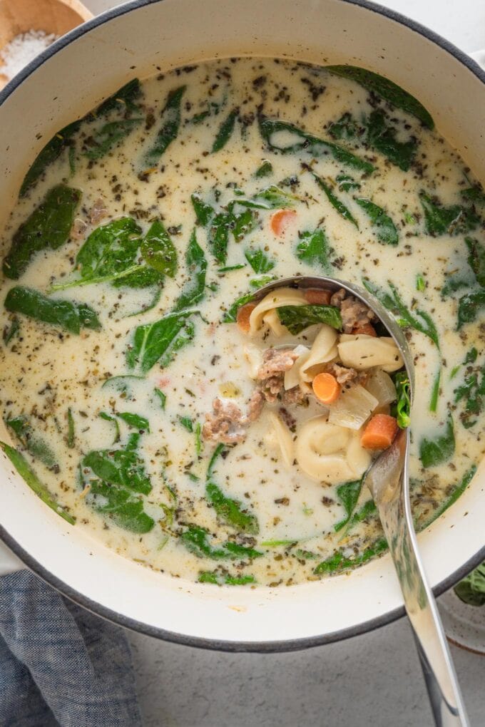 Close up of a pot full of creamy sausage tortellini soup with a ladle about to lift out a big spoonful to serve.